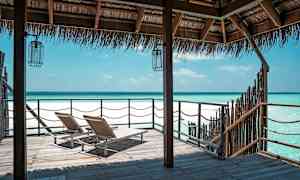 To liggestole på en træbro med udsigt over en klarblå kyst under et stråtag. (AI-genereret tekst)