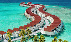 En række af stilfulde over-vand bungalows med røde tage på azurblåt vand. (AI-genereret tekst)