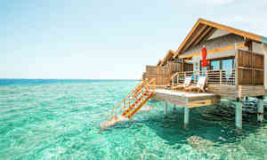 Fotografi af en bungalow på pæle over turkisvand. (AI-genereret tekst)