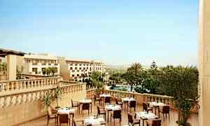 Hotellets udendørs terrasse med oplagte borde, omgivet af palmer og udsigt over landskabet. (AI-genereret tekst)