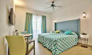 Et hotelværelse med en dobbeltseng, dekorative puder og et bord med to stole. (AI-genereret tekst)