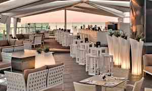 En lounge med moderne møbler, borde, sofaer og en bardisk under et overdækket tag. (AI-genereret tekst)