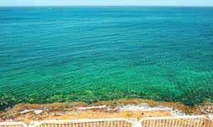 En udsigt over en klar blå hav med en stenstrand, set fra et sted med hvide rækværk. (AI-genereret tekst)