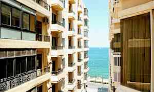 Billede af en by med høje bygninger på begge sider af en smal gade, med havet synligt i baggrunden. (AI-genereret tekst)