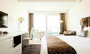 Et hotelværelse med en stor seng, skrivebord, stol, sofa og altan med glasdøre. (AI-genereret tekst)