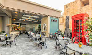 Udendørsområde med borde og stole på en café. Der er en rød telefonboks og grøn planteudsmykning. (AI-genereret tekst)