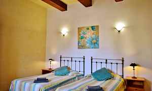 Et soveværelse med to enkeltsenge, væglamper og et blåt blomstermaleri på væggen. (AI-genereret tekst)