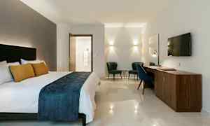 Hotelværelse med dobbeltseng, skrivebord, to lænestole og vægmonteret TV. (AI-genereret tekst)