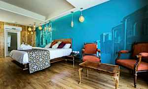 Et hotelværelse med en stor seng, dekorativ vægmaleri, træindretning og to røde lænestole foran et bord. (AI-genereret tekst)