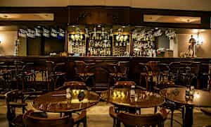 En elegant bar med træmøbler og bordopsætninger med stole i forgrunden. (AI-genereret tekst)