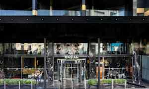 Forsiden af et hotel med glasdøre og en dekorativ sølvfarvet girafstatue ved siden af indgangen. (AI-genereret tekst)