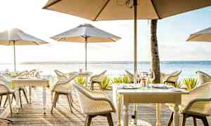 En udendørs restaurant med borde og parasoller ved havet. (AI-genereret tekst)