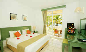 Hvidt værelse med en stor seng, dekorative blomsteblade på dynen og terrasseudgang mod en palmehave. (AI-genereret tekst)