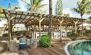 En lounge ved en pool på en tropisk resort med siddepladser og en bar under træbjælker. (AI-genereret tekst)