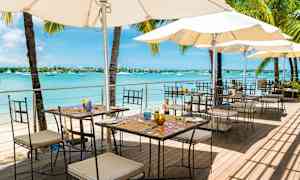 Udendørs restaurant ved havet med borde, stole og parasoller. (AI-genereret tekst)