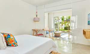 Et lyst hotelværelse med en seng, skrivebord og siddegruppe. Store vinduer med udsigt til en frodig have. (AI-genereret tekst)