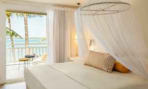 En lys hotelsuite med en himmelseng og udsigt over havet fra altanen. (AI-genereret tekst)