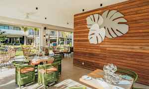 En udendørsrestaurant med grønne møbler og en vægdekoration af store blade. (AI-genereret tekst)