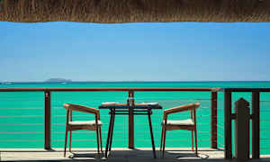 Et dækket bord med to stole på en terrasse med havudsigt. (AI-genereret tekst)