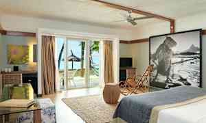 Et hotelværelse med moderne interiør, glasdøre der åbner ud til strand og palmer. (AI-genereret tekst)