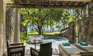 En terrasse med siddepladser og liggestole ved siden af en lille pool, omgivet af planter og med udsigt mod stranden og palmetræer. (AI-genereret tekst)