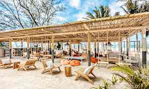 Strandbar med siddepladser og hængekøjer under et trætag. (AI-genereret tekst)