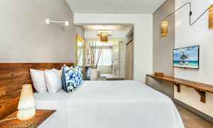 Billede af et moderne hotelværelse med træmøbler, seng med hvide lagner og farverige puder, og et stort vindue i baggrunden. (AI-genereret tekst)