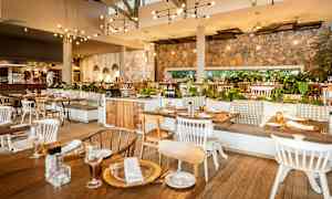 Indendørs interiør af en restaurant med træborde og stole, stenvægge, hængende lamper og grønne planter som dekoration. (AI-genereret tekst)