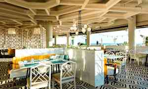 En moderne restaurant med geometrisk mønstret gulv, lyse møbler og store panoramavinduer med udsigt over havet. (AI-genereret tekst)