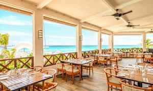 Restaurant med terrasse med borde og stole, udsigt over havet og stranden. (AI-genereret tekst)