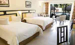 Billede af et hotelværelse med to store senge, siddeområde og et bord foran store vinduer med udsigt til en pool. (AI-genereret tekst)