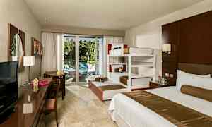 Hotelværelse med senge, skrivebord og udsigt til en altan med grønt. (AI-genereret tekst)