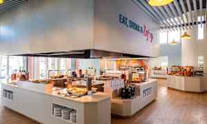 En cafeteria med selvbetjening, hvor mad præsenteres på diske, og brødudvalg kan ses på hylder. (AI-genereret tekst)