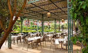 En udendørs spisested med borde og stole under et trælister tag. (AI-genereret tekst)