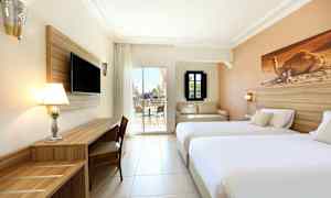 Billede af et hotelværelse med to senge, TV, skrivebord og en siddegruppe samt udsigt til en terrasse. (AI-genereret tekst)