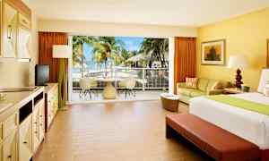 Hotelværelse med lyst interiør og udsigt til en terrasse med palmer og hav. (AI-genereret tekst)