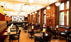Billede af en restaurantinteriør med træborde og stole, store vinduer og hængende lamper i loftet. (AI-genereret tekst)