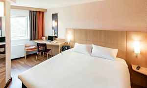 Hotelværelse med en dobbeltseng, et skrivebord med en stol og et vindue. (AI-genereret tekst)