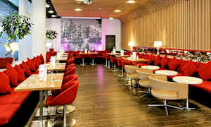 Stemningsfuld restaurant med røde siddepladser, små borde og en baggrundsvæg med et sort-hvidt bybillede. (AI-genereret tekst)