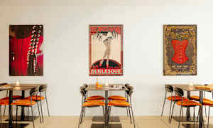 Billede af et cafémiljø med borde og stole samt burlesque-inspirerede plakater på væggen. (AI-genereret tekst)