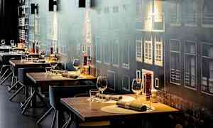 Flere dækkede restaurantborde med glas og bestik, mod en væg med facademotiv. (AI-genereret tekst)