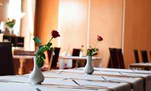 Et elegant dækket spisebord pyntet med en hvid vase, der indeholder en enkelt rød rose. (AI-genereret tekst)