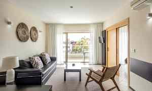 En moderne stue med sofa, træstol og adgang til altan via glasdøre. (AI-genereret tekst)