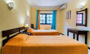 Et hotelværelse med to enkeltsenge, et vægspejl, skrivebord og vindue med farverige gardiner. (AI-genereret tekst)