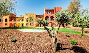 Bygninger malet i gul og rød med arkader, omgivet af træer og anlagte grønne områder. (AI-genereret tekst)