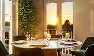 Et dækket spisebord ved vinduet med udsigt over solnedgang. (AI-genereret tekst)