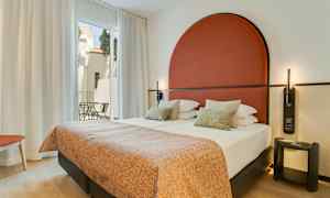 Moderne hotelværelse med dobbeltseng, rødt sengegærde og store vinduer mod en altan. (AI-genereret tekst)