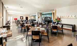 En lys og moderne restaurant med borde og stole pænt arrangeret, friske blomster og store vinduer. (AI-genereret tekst)