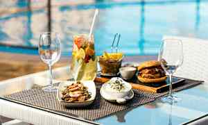 Mad på et bord ved poolen, bestående af salat, burger, pommes frites og drikke. (AI-genereret tekst)