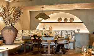 Et stilfuldt restaurantbord omgivet af stole og bænke med geometriske mønstrede puder. (AI-genereret tekst)